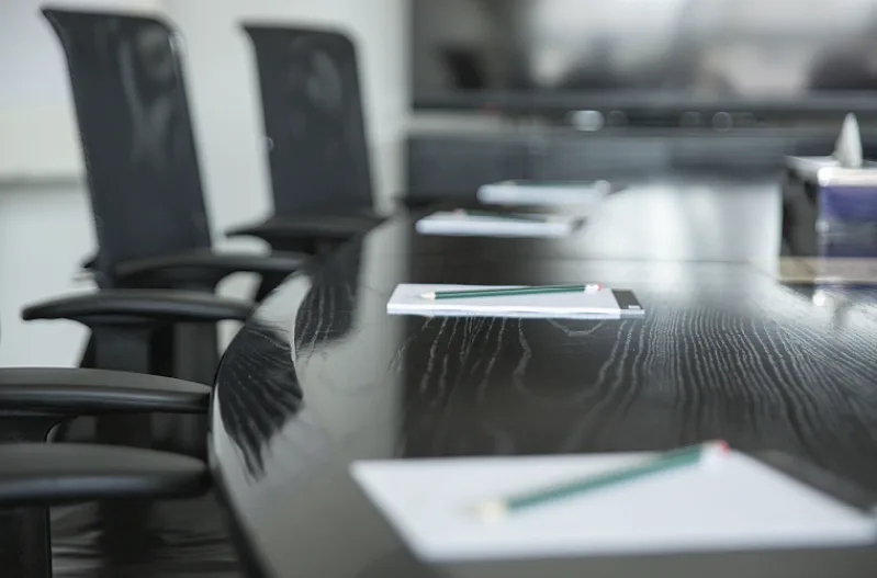 A large table in a meeting room with several notepads and chairs